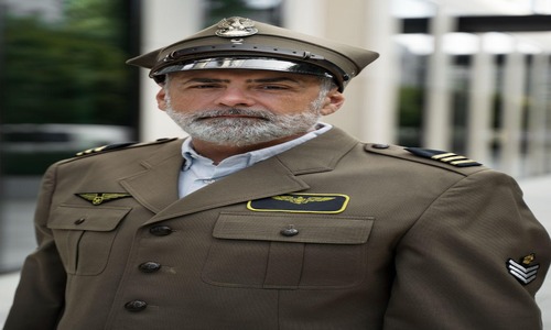Man in formal military-style uniform with rank insignia and aviation badges, standing outdoors.









