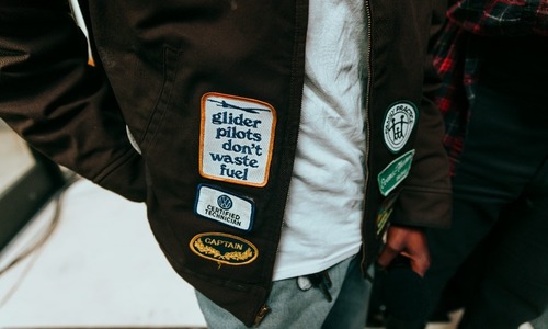 Person wearing a brown jacket with various embroidered patches, including one saying “glider pilots.”