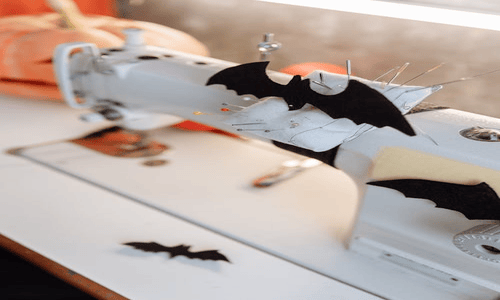 Close-up of a sewing machine decorated with black bat patches for a creative Halloween project.