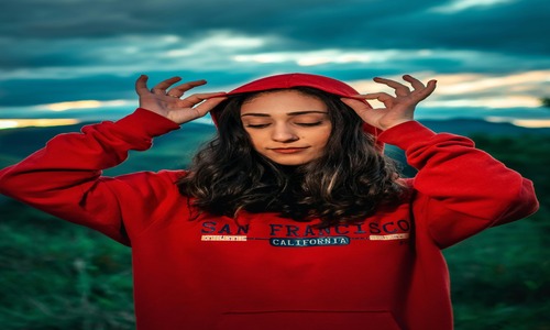 Young woman in a red hoodie enjoying a calm outdoor moment in nature.