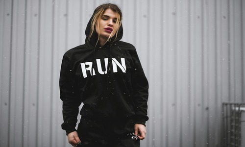 Woman in black & white “RUN” printed hoodie posing confidently in urban streetwear fashion.