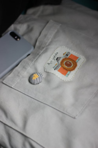 A white canvas pocket featuring a camera patch and a striped heart button.