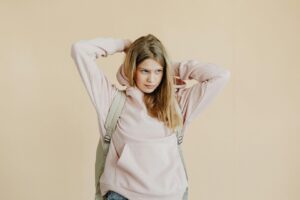 Young woman in a pink hoodie pulling back her hair, wearing a backpack.