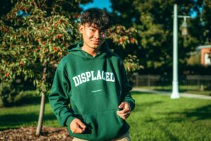 Young man smiling outdoors wearing a green hoodie with 'DISPLACED' text