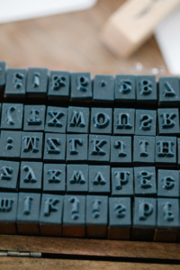 A collection of small, black rubber alphabet stamps arranged in a wooden box.