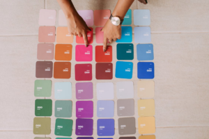 Hands pointing to a grid of various colorful fabric or color swatches on a floor.