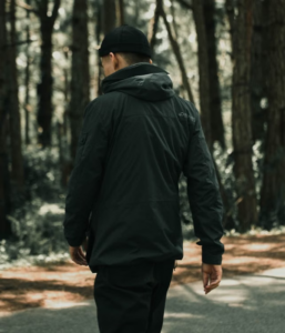 Back view of a person in a black dark jacket and cap walking through a wooded path.