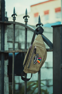 Green corduroy fanny pack with a UFO patch hanging on a wrought iron fence.