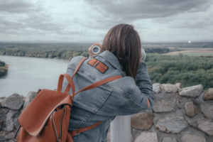 Person in a denim jacket with a band patch looking through scenic view binoculars.