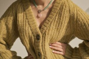 Close-up of a person wearing a knit yellow cardigan sweater and a beaded heart necklace.
