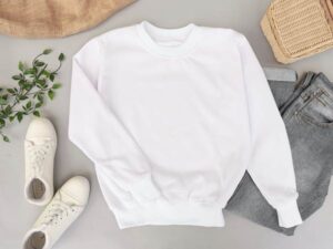 White crewneck sweatshirt displayed in a flat lay style with white sneakers, jeans, and decorative items.
