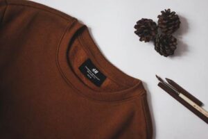 Brown crewneck sweatshirt neatly laid out next to pine cones and paintbrushes.