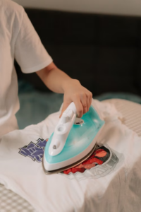 Person pressing a blue and white clothing iron onto a patch on a white shirt.